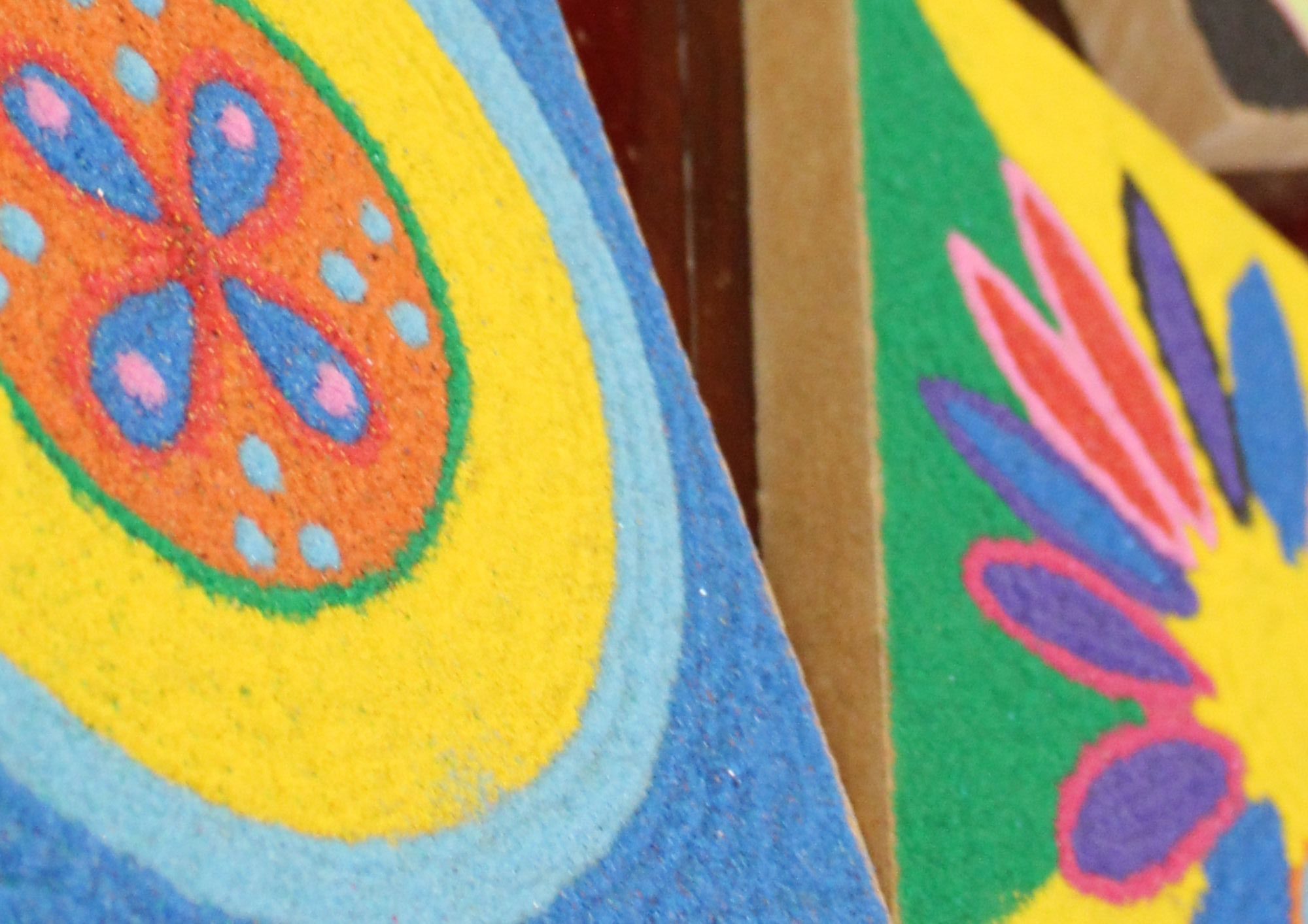 sand art: circular coloured rings, blue, yellow, orange, with flower pattern in middle