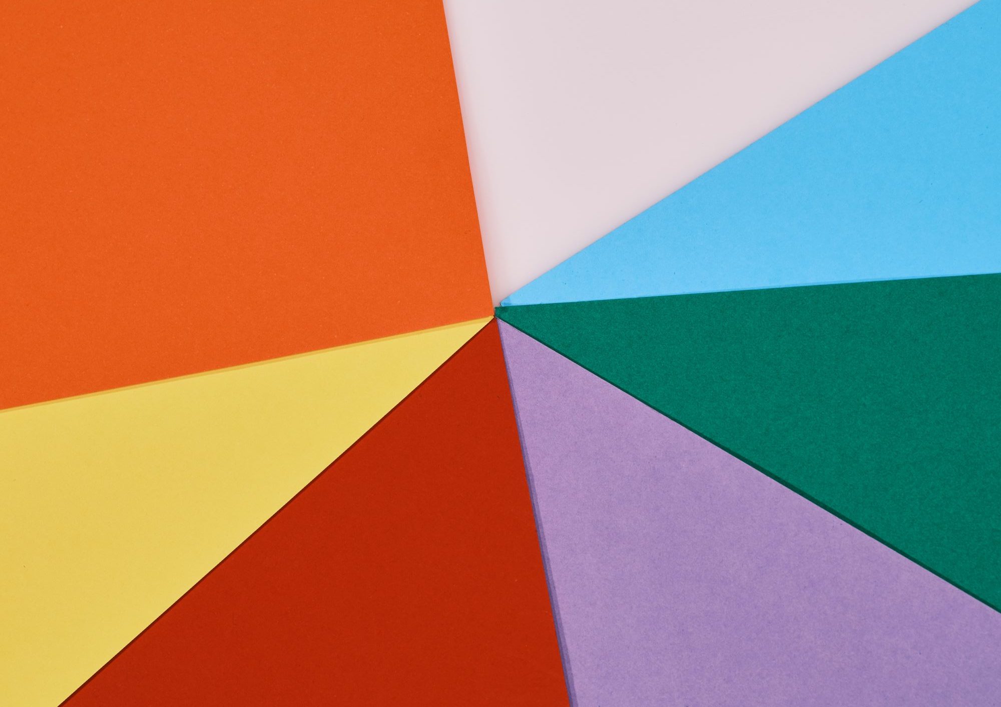 the corners of coloured card all pointing towards the centre of the image. There's orange, off white, light blue, dark green, purple, red and yellow